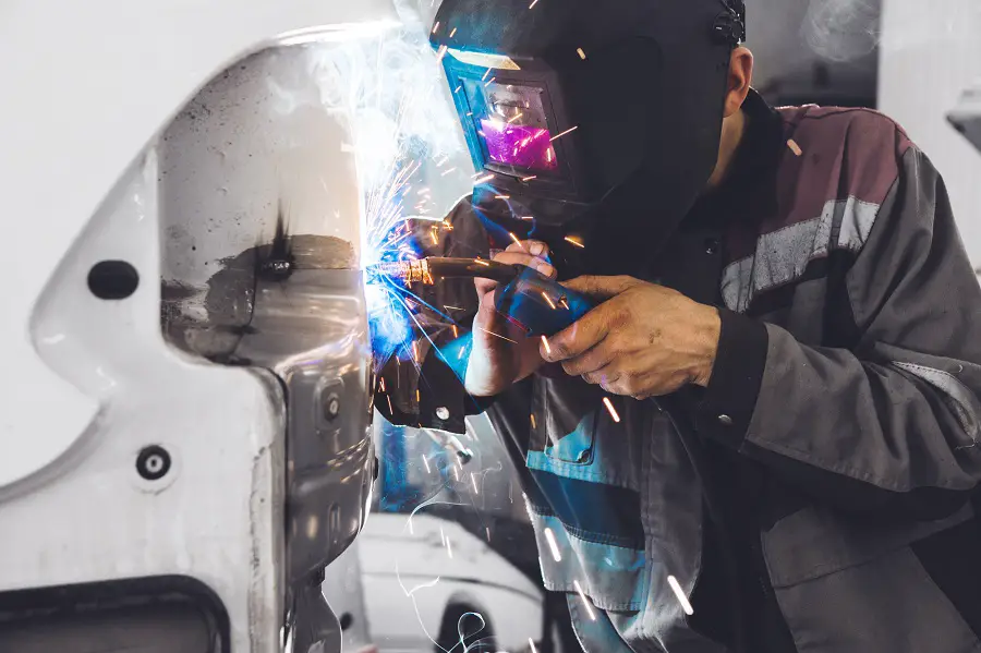 Welder welds on car with auto darkening welding helmet
